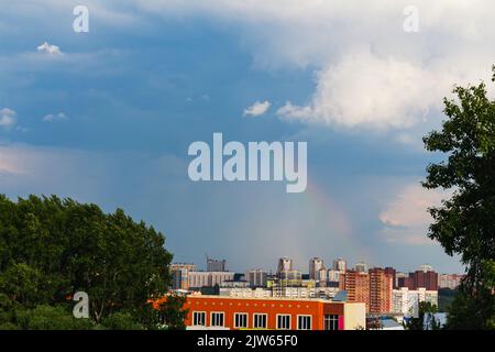 Schöner Regenbogen, der von stürmischem Himmel umrahmt wird, erscheint plötzlich über dem Wohngebiet Tomsk, Russland. Platz für Text kopieren. Stürmisches Wetter, schöne Landschaft. n Stockfoto