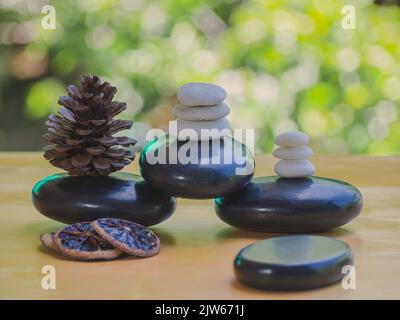 Balance- und Wellness- oder Gesundheitskonzept mit Haufen schwarzer Spa-Steine auf Holz und Spitzen blühenden Lavendels mit Aromatherapie. Seitenansicht und Landschaft Stockfoto