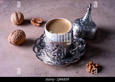 Kleine schöne traditionelle Tasse mit türkischem Kaffee steht auf einem beigen Hintergrund. Walnüsse liegen neben einer Kaffeetasse. Selektiver Fokus. Stockfoto