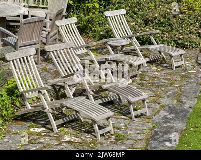 Vier alte Holzliegen auf der Terrasse aus Stein, Colonsay House Gardens, Isle of Colonsay, Schottland, Großbritannien. Stockfoto