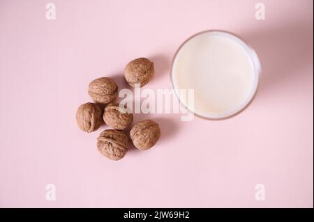 Flaches Trinkglas mit gesunder pflanzlicher Milch und Walnüssen auf rosa Hintergrund. Speicherplatz kopieren. Gesunde Lebensmittel trinken Stockfoto