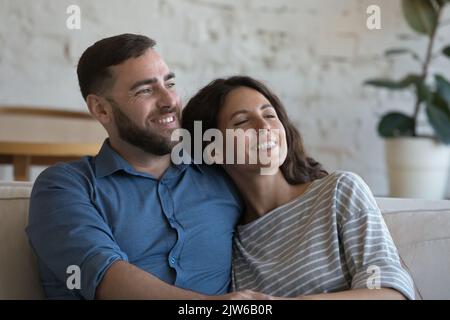 Ein glückliches, liebevolles Paar, das sich auf dem Sofa entspannt, lächelt und in die Ferne starrt Stockfoto