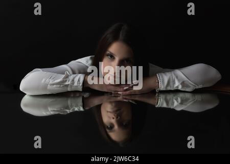 Low-Key-Porträt der Brünette junge Frau auf dem Spiegel liegend und Blick auf die Kamera. Horizontal. Stockfoto