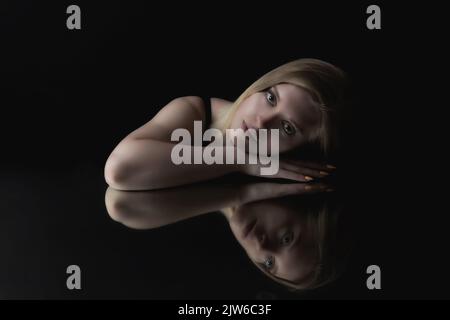 Low-Key-Porträt der blonden jungen Frau auf dem Spiegel liegt auf die Kamera anhaken. Horizontal. Stockfoto