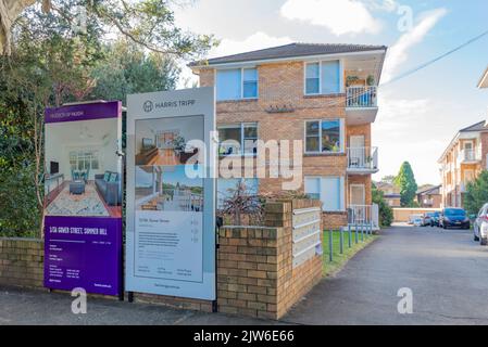 For Sale-Schilder an der Vorderseite eines blonden Wohnblocks aus Ziegelsteinen aus den 1960er Jahren in Summer Hill, Sydney, New South Wales, Australien Stockfoto