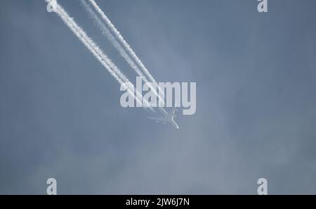 Airliner mit einem Trail hoch am blauen Himmel. Dampfspur eines Düsenflugzeugs. Reisen mit Flugzeugen. Stockfoto