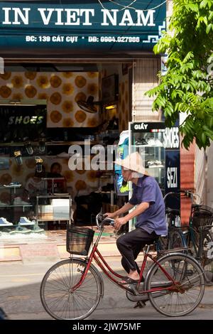 Mann mit Bambushut auf dem Fahrrad am vietnamesischen Laden Hai Phong, Vietnam vorbei Stockfoto