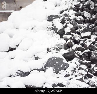 Kohle im Kraftstofflager mit Schnee bedeckt. Verkauf von Kohle im Winter. Kohle für die Beheizung von Häusern und Industrie. Kraftstoffzusammensetzung im Winter. Stockfoto