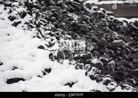 Kohle im Kraftstofflager mit Schnee bedeckt. Verkauf von Kohle im Winter. Kohle für die Beheizung von Häusern und Industrie. Kraftstoffzusammensetzung im Winter. Stockfoto