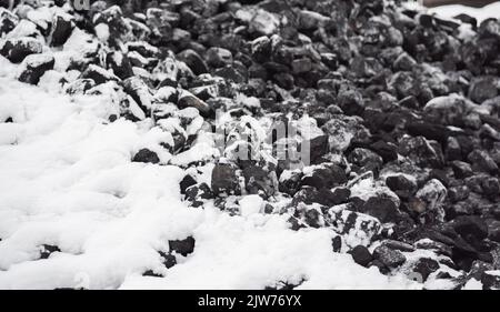 Kohle im Kraftstofflager mit Schnee bedeckt. Verkauf von Kohle im Winter. Kohle für die Beheizung von Häusern und Industrie. Kraftstoffzusammensetzung im Winter. Stockfoto