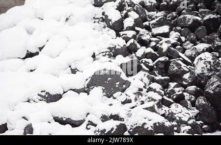 Kohle im Kraftstofflager mit Schnee bedeckt. Verkauf von Kohle im Winter. Kohle für die Beheizung von Häusern und Industrie. Kraftstoffzusammensetzung im Winter. Stockfoto