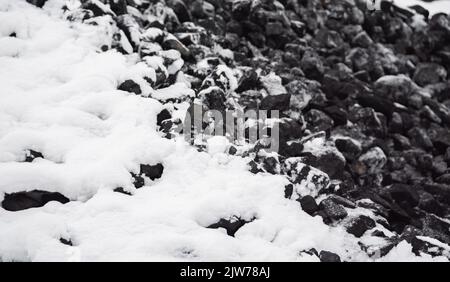 Kohle im Kraftstofflager mit Schnee bedeckt. Verkauf von Kohle im Winter. Kohle für die Beheizung von Häusern und Industrie. Kraftstoffzusammensetzung im Winter. Stockfoto