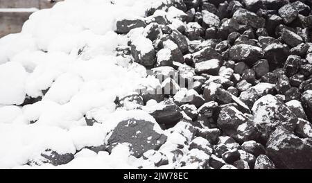 Kohle im Kraftstofflager mit Schnee bedeckt. Verkauf von Kohle im Winter. Kohle für die Beheizung von Häusern und Industrie. Kraftstoffzusammensetzung im Winter. Stockfoto