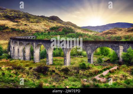 Schottland Landschaft - Glenfinnan Zug Viadukt bei dramatischem Sonnenuntergang mit Sonne, Großbritannien Stockfoto