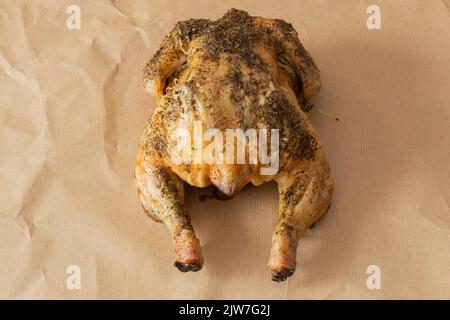 Das ganze Huhn ist mit gemischten Kräutern überzogen und im Ofen geröstet. Auf einem braunen Papierhintergrund Stockfoto