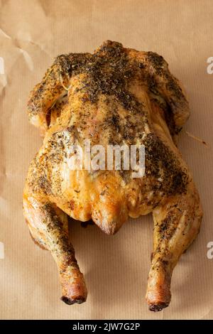 Das ganze Huhn ist mit gemischten Kräutern überzogen und im Ofen geröstet. Auf einem braunen Papierhintergrund Stockfoto