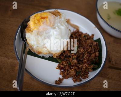 Pad Krapow MOO - Thailändisches Basilikum aus Schweinefleisch mit Reis und gebratenem Ei im Hintergrund. Thailändische Küche Gericht mit gehacktem Schweinefleisch, Basilikum, Soja und Austernsaucen. Thai Food Co Stockfoto