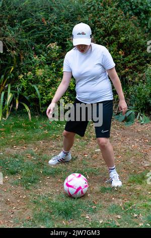 Frau in Ellesse Cap und Nike Shorts, die Fußballfähigkeiten im Park üben Stockfoto