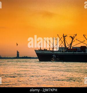 New York, 1980s, Frachtschiff, Liberty Island in der Ferne, Sonnenuntergang, obere New York Bay, New York City, NYC, NY, USA, Stockfoto