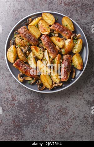 Roastbeef-Brötchen mit gebackenen Kartoffelkeilen und Pilzen, die auf dem Teller in der Nähe auf dem Tisch serviert werden. Vertikale Draufsicht von oben Stockfoto
