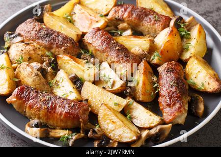 Gebackene Rinderbrötchen mit Kartoffelkeilen, Pilzen und Thymian auf dem Teller in der Nähe auf dem Tisch. Horizontal Stockfoto