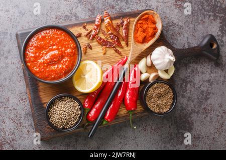 Arabische Küche Harissa Paste besteht aus heißen Chilischoten, Knoblauch und Gewürzen auf der Schüssel auf Holzbrett mit Zutaten Nahaufnahme. Horizontal oben Stockfoto