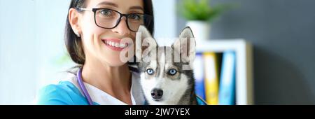 Lächelnde Tierärztin mit Hund in den Armen in der Klinik Stockfoto