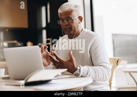 Leitender Geschäftsmann, der während eines Online-Meetings in seinem Heimbüro spricht. Leitender Geschäftsmann, der während der Arbeit eine Videokonferenz mit seinen Kollegen führt Stockfoto