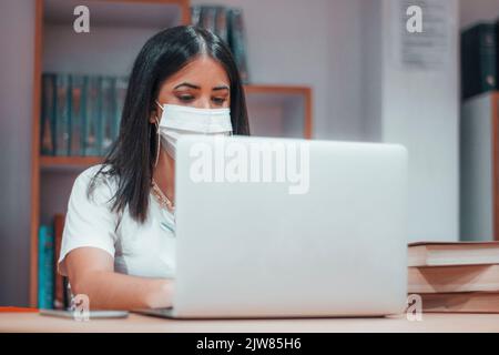Eine kaukasische Frau, die in einer Bibliothek auf einem Laptop tippt Stockfoto