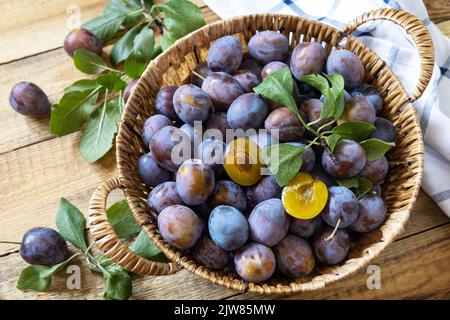 Obst Hintergrund, Bio-Früchte. Stillleben Essen. Korb mit frischen blauen Pflaumen auf einem rustikalen Holztisch. Stockfoto