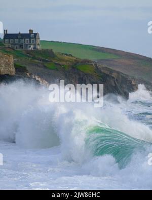 Massive Wellen schlagen in den Porthleven Strand mit Tye Rock Manor auf der Klippe dahinter. Stockfoto