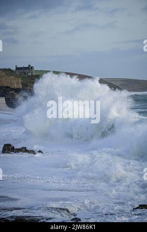 Massive Wellen schlagen in den Porthleven Strand mit Tye Rock Manor auf der Klippe dahinter. Stockfoto