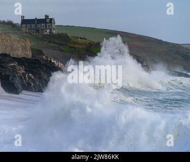 Massive Wellen schlagen in den Porthleven Strand mit Tye Rock Manor auf der Klippe dahinter. Stockfoto