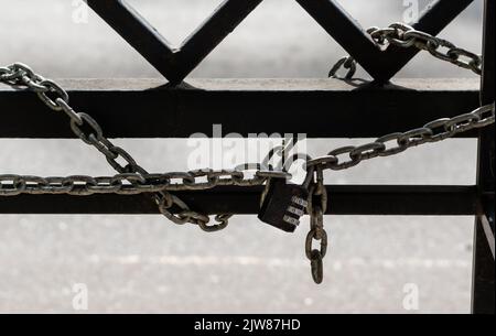 Metallschloss mit Nahaufnahme des manuellen Codes und Kette auf hellem unscharfem Hintergrund mit Metallzaun Stockfoto