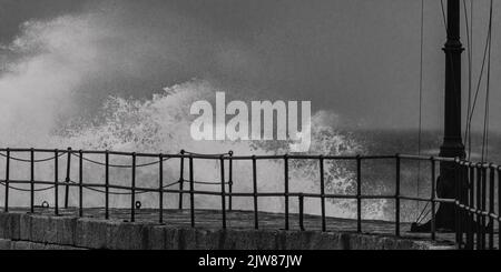 Als ein Sturm die Küste von Cornwall trifft, nimmt der Pier am Hafen von Porthleven die Kraft der Wellen auf, während sie hart treffen. Stockfoto