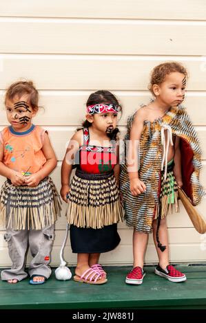 Eine kleine Gruppe von Maori-Kindern, die in ihrem traditionellen Tanzkleid gekleidet waren, beobachtete das kulturelle Tanzkonzert ihrer Eltern für Besucher des New Stockfoto