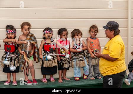 Eine kleine Gruppe von Maori-Kindern, die in ihrem traditionellen Tanzkleid gekleidet sind, und ihre Lehrerin beobachten das kulturelle Tanzkonzert ihrer Eltern Stockfoto