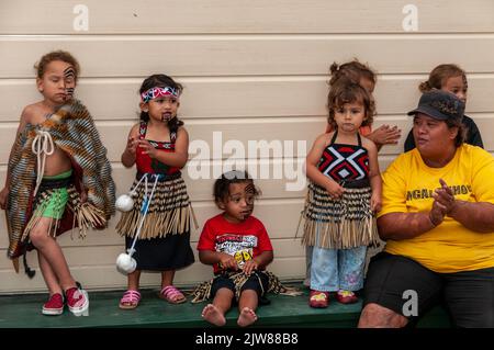 Eine kleine Gruppe von Maori-Kindern, die in ihrem traditionellen Tanzkleid gekleidet sind, und ihre Lehrerin beobachten das kulturelle Tanzkonzert ihrer Eltern Stockfoto