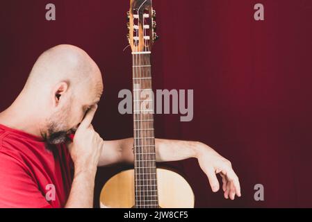 Saiteninstrument. Reifer charismatischer männlicher Gitarrist. Kerl mit Bart hält Gitarre. Bärtiger Mann in einem roten Hemd. Musik-Performer von Musik. Stockfoto