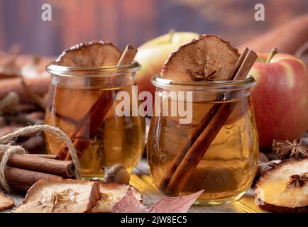Glas Apfelwein mit Zimtstange und getrockneten Apfelchips mit herbstlichem Hintergrund Stockfoto