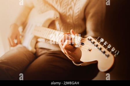 Ein Mann in einem weißen Pullover spielt an einem sonnigen Morgen Rockmusik auf einer weißen E-Gitarre. Aufführen von Musik auf einer sechsssaitigen Gitarre. Kunst und Inspiration. Stockfoto