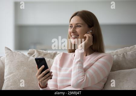 Fröhliche Smartphone-Benutzerin Frau, die den kabellosen Kopfhörer im Ohr berührt Stockfoto
