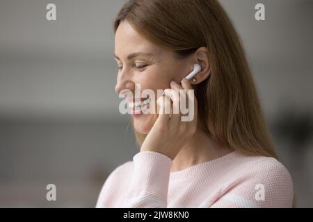 Ein glücklicher, hübscher Benutzer mit einem tausendjährigen Ohrhörer, der schnurlose Ohrhörer im Ohr anfasst Stockfoto