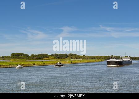 Rotterdam, Niederlande - August 2022: Gewerblicher Barge mit zwei kleinen Segelbooten. Kontrastkonzept Stockfoto