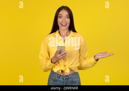 Glückliche Frau Mit Handy Lächelt Kamera, Gelber Hintergrund Stockfoto