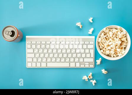 Eine Schüssel Popcorn, eine Tastatur und eine Dose Getränk auf blauem Hintergrund. Stockfoto