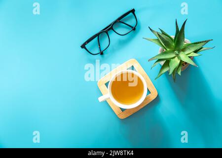 Tasse Tee, Blumentopf und Gläser auf blauem Hintergrund, flach liegend. Stockfoto
