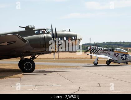 B-17 'Sally B' startet ihre Motoren für ihre Sommerflugschau auf der Duxford Summer Airshow am 23.. Juli 2022, flankiert von einem alten P-51 Mustang Fighter Stockfoto