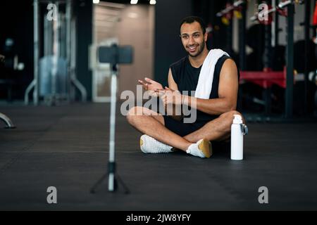 Black Young Fitness Coach Aufnahme Video Im Fitnessstudio Mit Smartphone Auf Stativ, Stockfoto