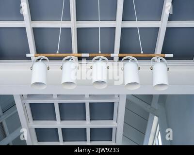 Fünf Scheinwerfer hängen im Café. Moderne Deckenlampen unter dem stilvollen Gebäude im Wohnzimmer des weißen Hauses. Spanndecke w Stockfoto